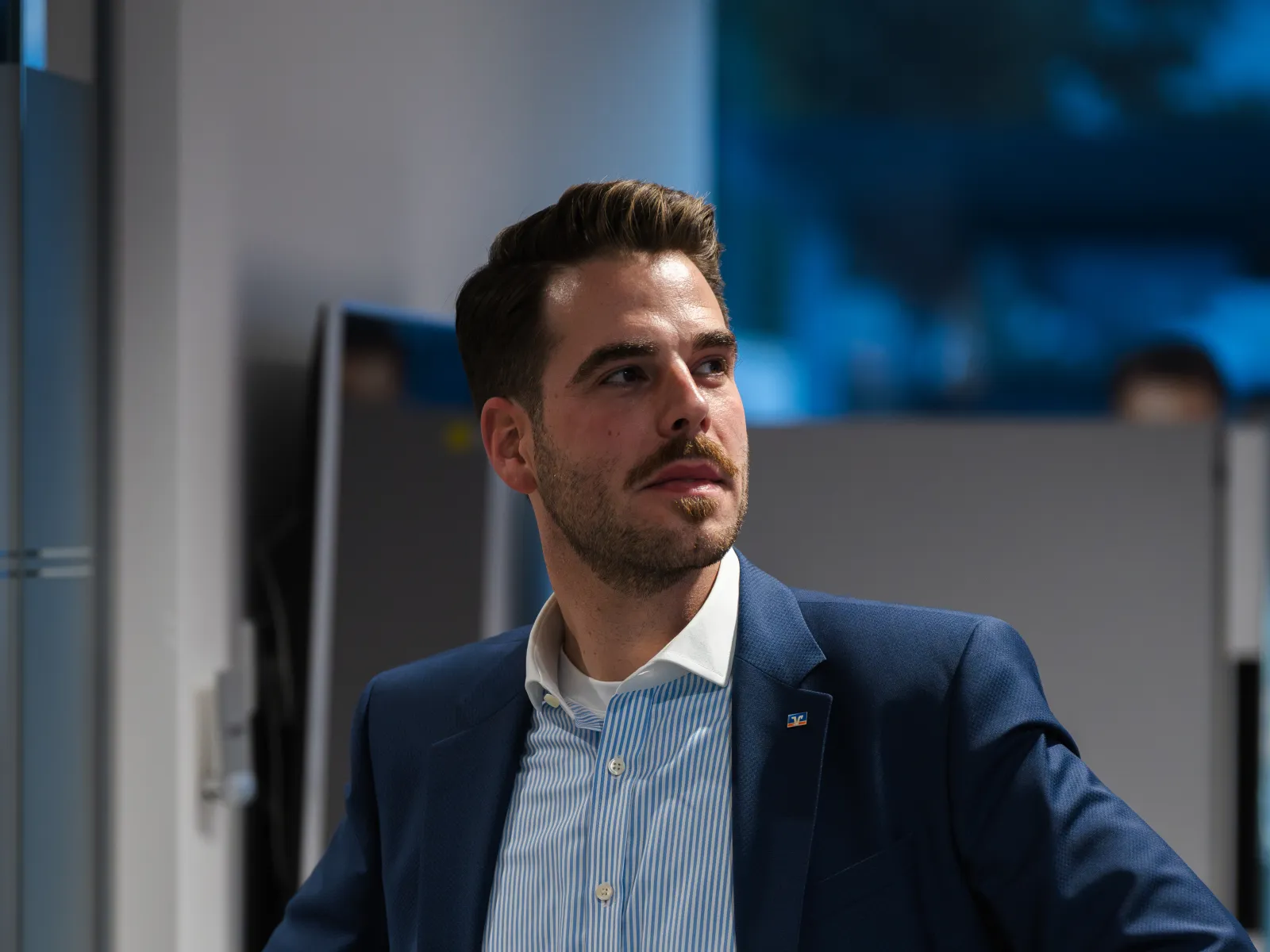 Ein junger Kollege im blauen Anzug steht im Foyer der Hauptstelle und blickt zur Seite